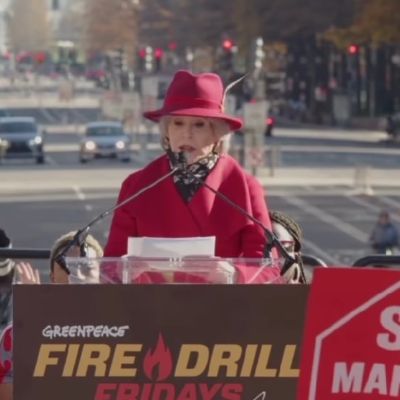 Jane Fonda is addressing the crowd, speaking through the podium as she is wearing a red jacket and a red hat.